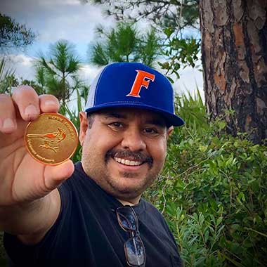 Man in Florida Gators hat holding up a coin.