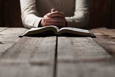 Hands clasped on religious text.