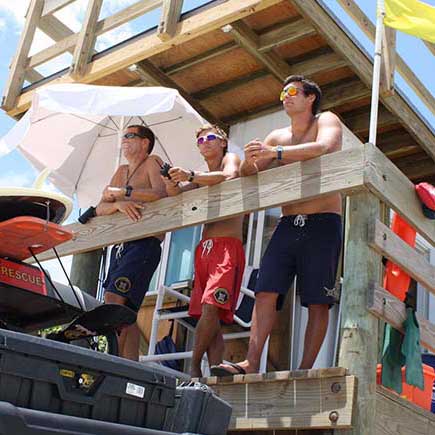 3 lifeguards overlooking beach goers.