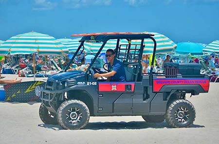 An Ocean Rescue lifeguard driving all-terrain vehicle patrolling the beach in Cocoa Beach.