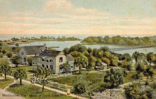 View of Crane Creek, early 1900s. 2 houses are surrounded by palm trees with a bridge crossing the creek in the background.