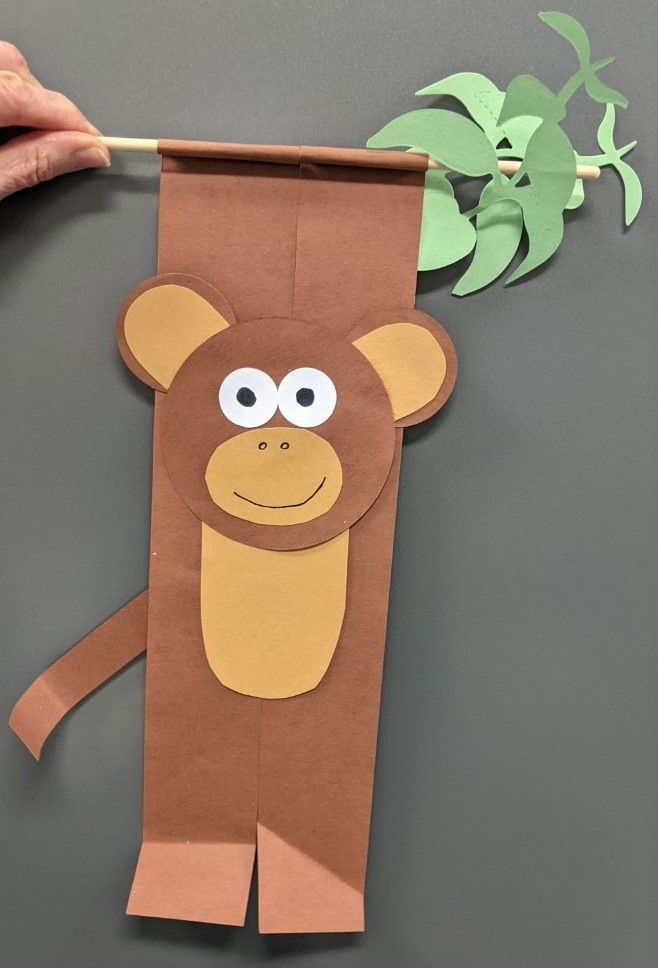 Monkey made of paper, holding on to a craft stick with paper leaves.