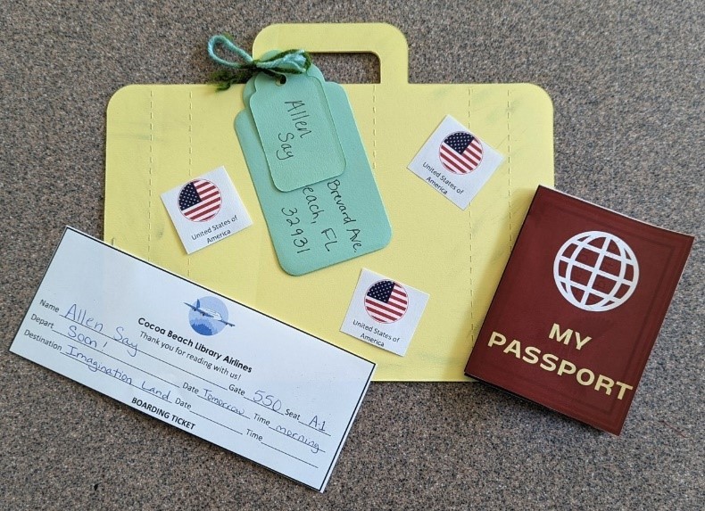 Passport A large 2D paper suitcase sits below a play passport and Cocoa Beach Library Airlines boarding pass. Luggage tags are tied to the paper suitcase with yarn.
