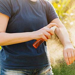 person spraying arm with mosquito repellent