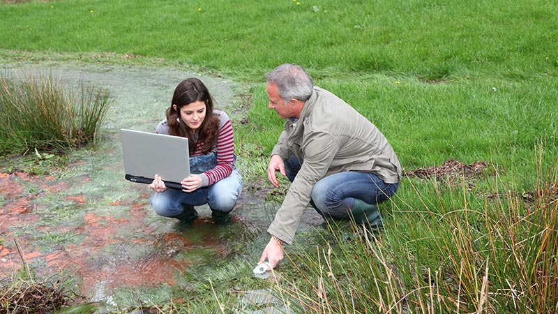 2 scientists performing tests in a marshy area.