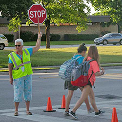 Crossing guard stopping traffic for 2 children crossing the street.
