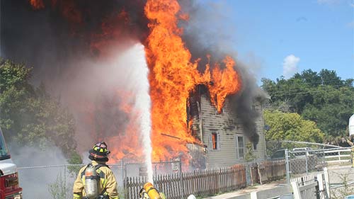 Firefighters spraying water on a buring house with a firehose.