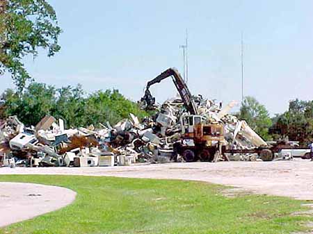 Backhoe digging through a large pile of scrap metal.