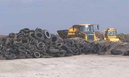 Dump truck and backhoe parked next to a large pile of used tires.