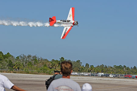 Airplane flying low with smoke trail at air show.